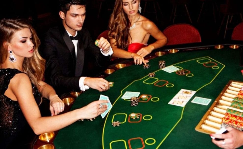 People sitting around a poker table, engaging in a game of poker, with poker chips, and cards, arranged on the table. 