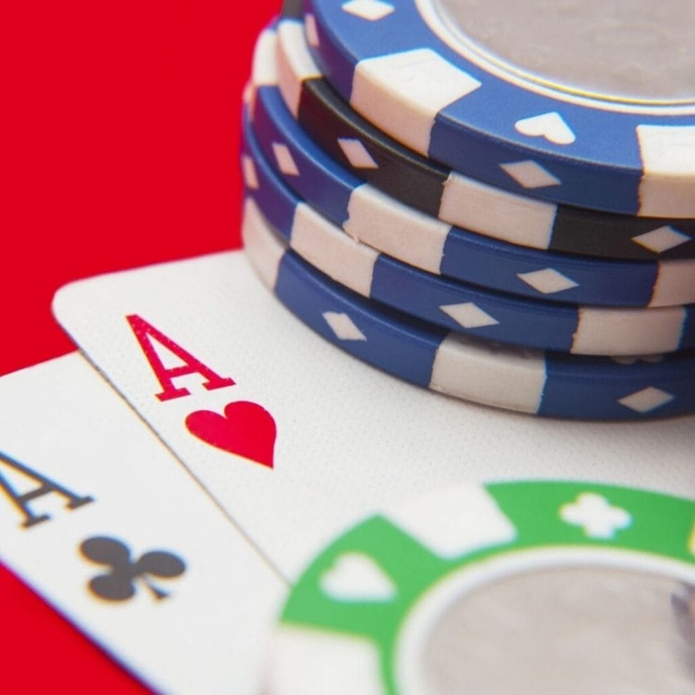 A close up of playing cards, and poker chips, on a red poker table.
