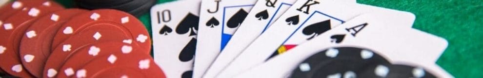 A close up of playing cards, and poker chips, on a poker table.