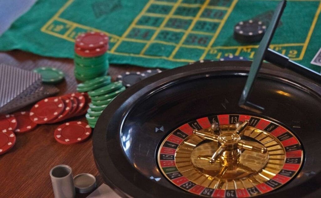 A roulette wheel, casino chips, and playing cards arranged on a roulette table.
