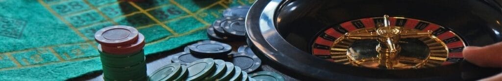 A closeup of a roulette wheel, and casino chips on a table.