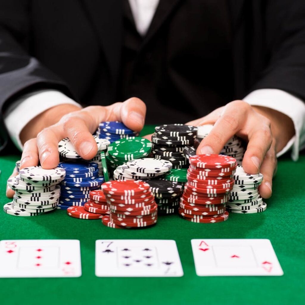 Hands shoving casino chips forward on a green felt table with playing cards.