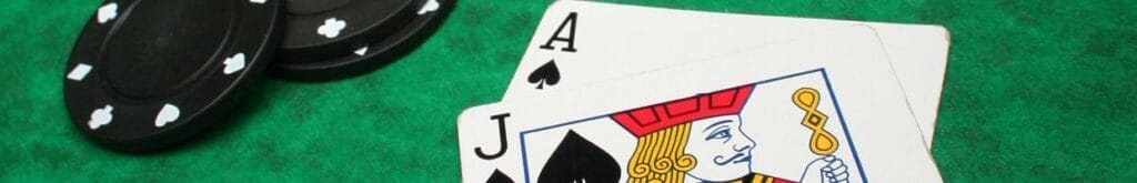 an ace and jack of spades playing cards on a green felt poker table next to three black poker chips