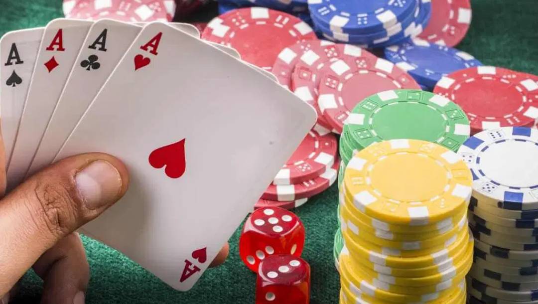 A poker player holding four aces in front of stacks of poker chips, scattered poker chips, and a pair of dice.