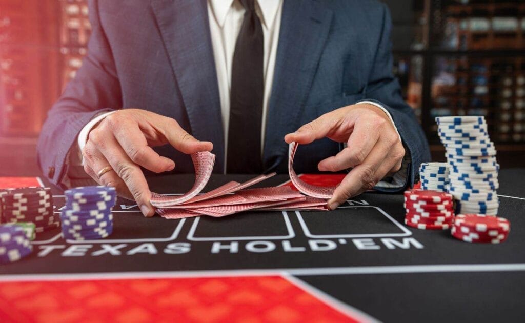 A man wearing a suit, shuffling cards at a poker table, with stacks of poker chips arranged in front of him. 