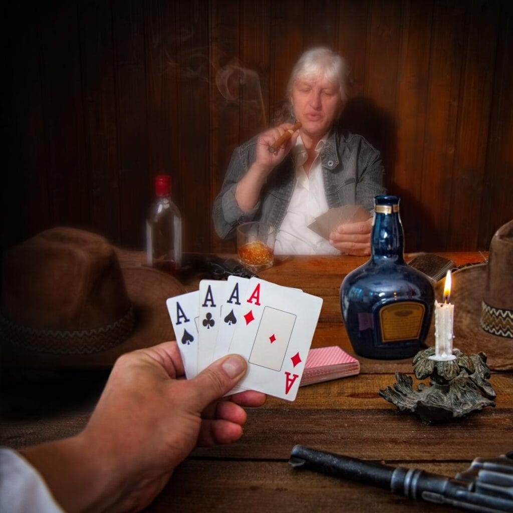 A hand holds four aces in a game of poker taking place in an old wild west saloon.