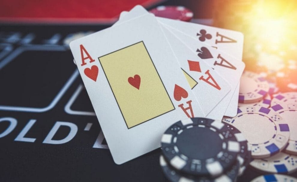 An ace of hearts, an ace of diamonds, an ace of spades, an ace of clubs, and white and black poker chips arranged on a poker table.