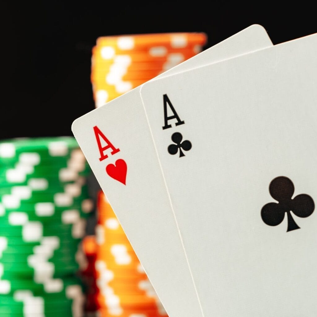 A close-up of a pair of aces with stacks of poker chips in the background.