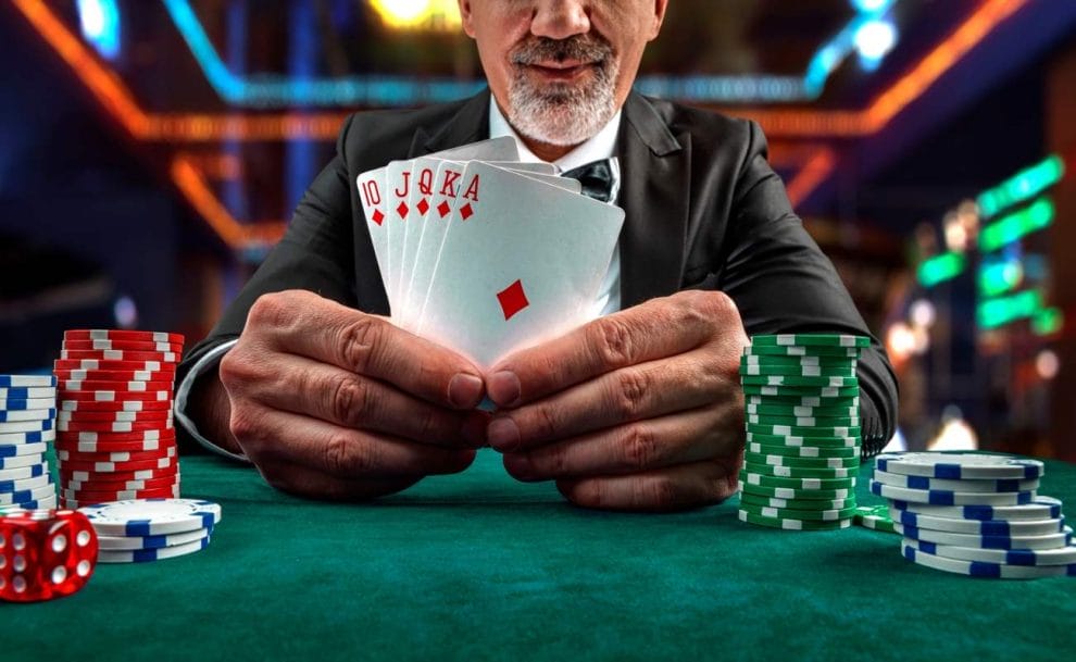 A man with a goatee holds a royal flush in diamonds