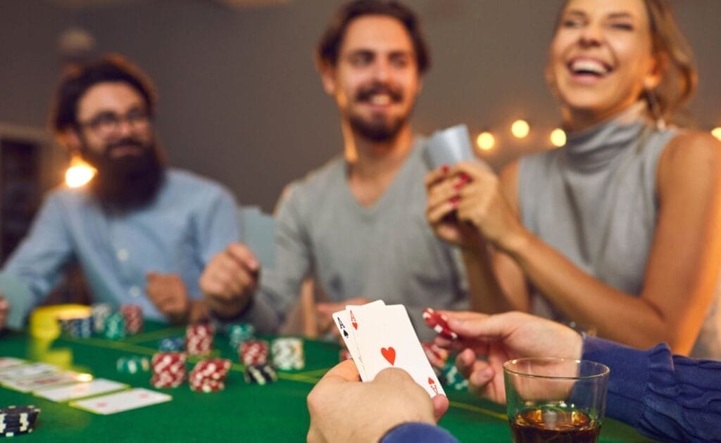 A man holding to ace playing cards at a poker table with friends.