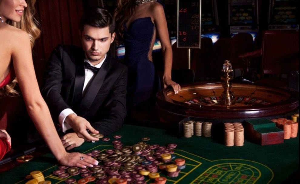 A glamorous casino with well-dressed people surrounding a casino table.
