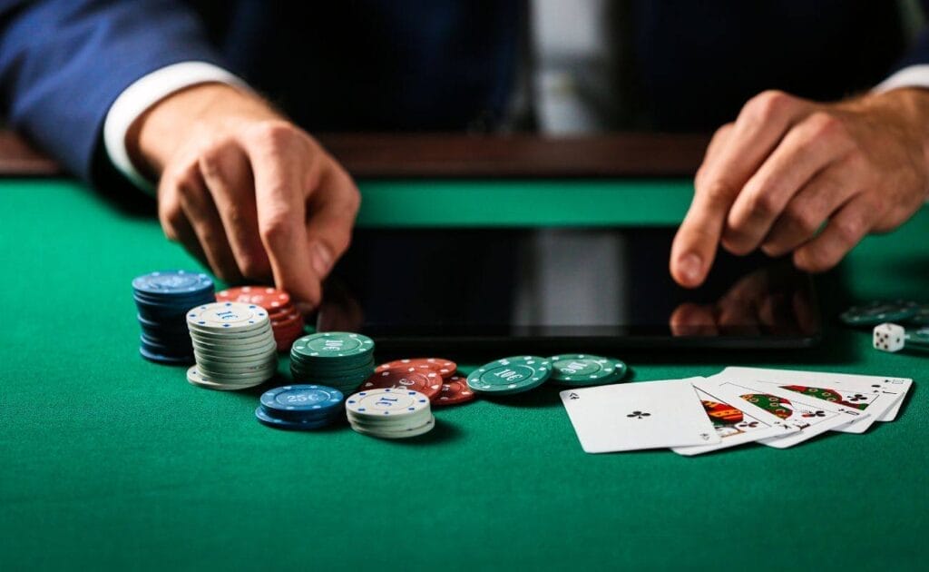 a man is sitting at a green felt poker table while working on an ipad with stacks of poker chips, playing cards and dice on the table in front of the ipad 