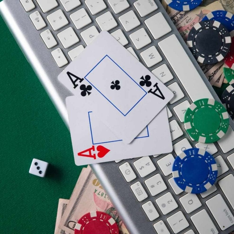 a pair of ace playing cards on a computer keyboard with poker chips scattered on and around it on a green felt poker table