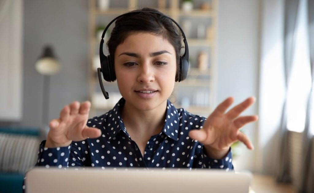 A woman wears a headset sitting in front of a laptop