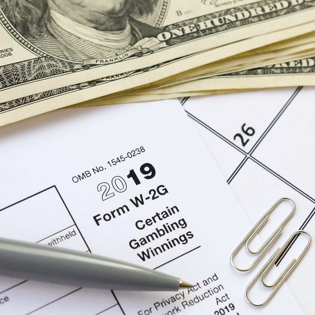 A grey pen, money, and paper clips on top of a tax form for gambling winnings.