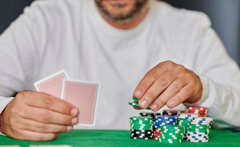 a person holding two playing cards above a green felt poker table with poker chips stacked on it 