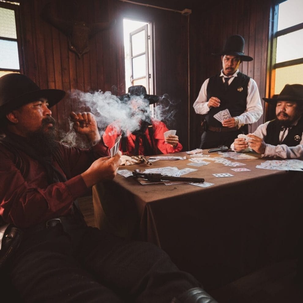 Cowboys sit around a table playing poker and smoking cigars