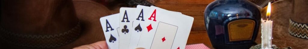 A hand holds four aces in a game of poker taking place in an old wild west saloon
