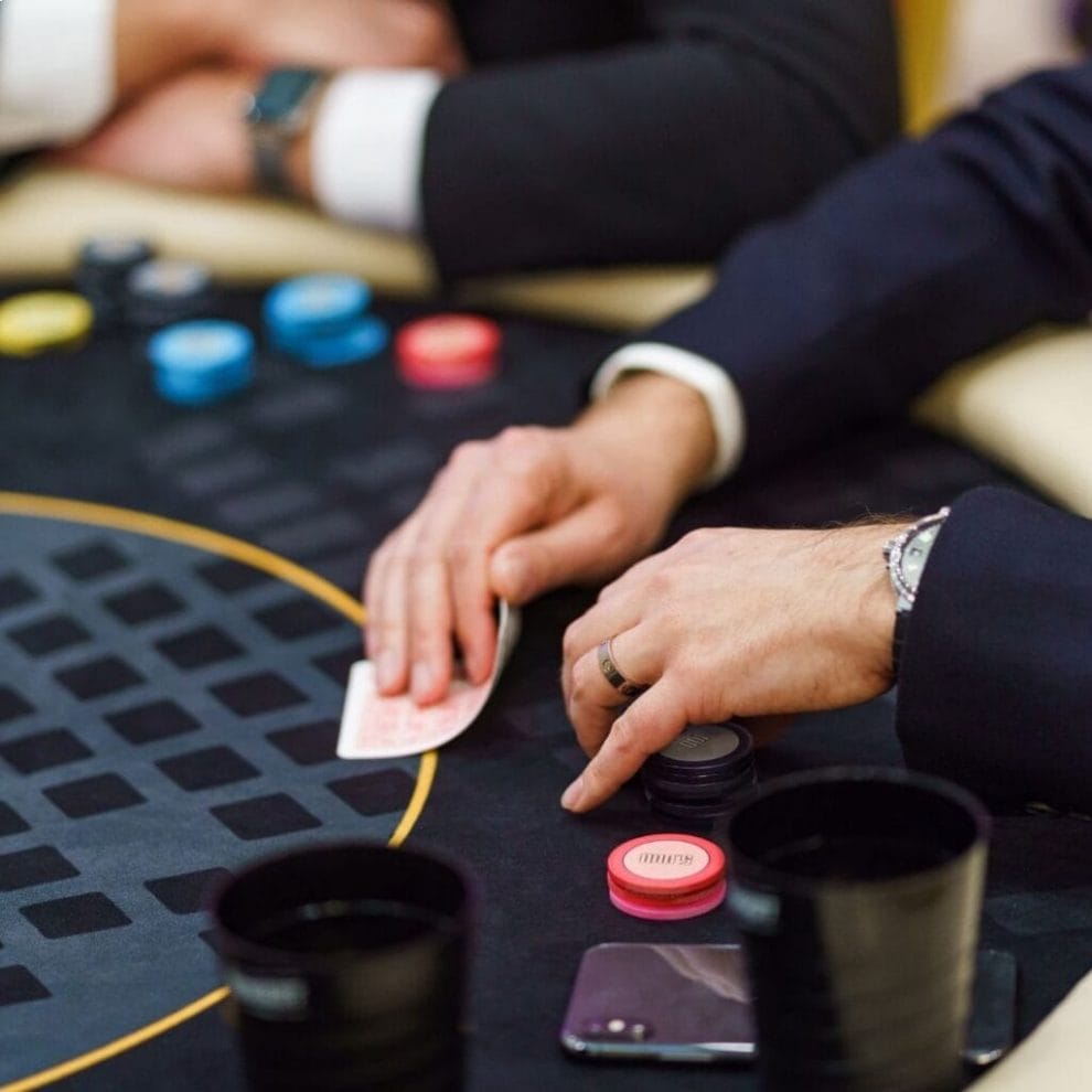 Man at a poker game examining his cards and hovering his hands over poker chips.