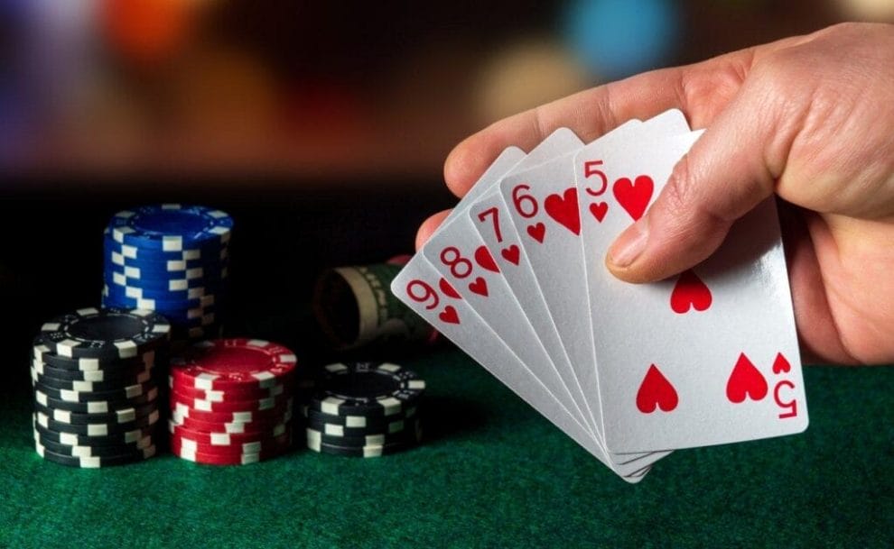 A poker player holds a straight flush. There are stacks of chips and a roll of cash in the background.