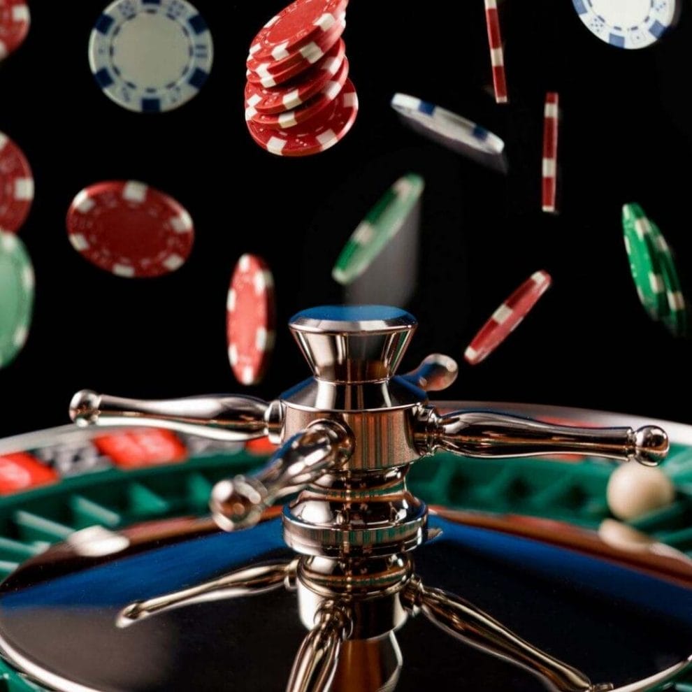 A closeup of casino chips being dropped onto a roulette wheel against a black background.