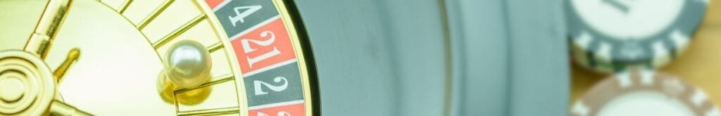 A closeup of a golden roulette wheel on a wooden table with two small stacks of casino chips in the background.