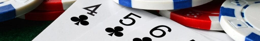 A close-up of poker cards next to scattered poker chips. The cards visible are 4, 5, and 6 of clubs.