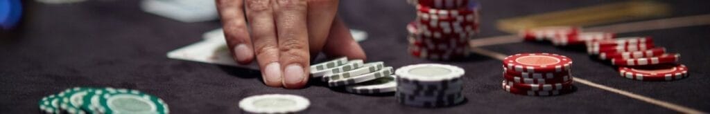 Hand placing poker chips in the center of the poker table, with additional chips scattered around.