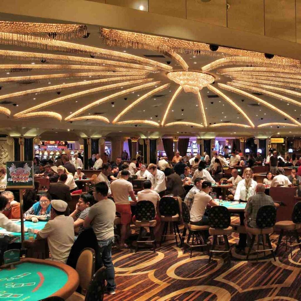 Casino hall with numerous players gathered around multiple poker tables.