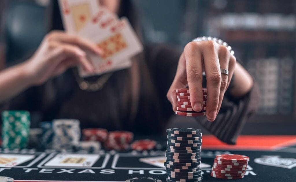 A person sitting at a poker table, holding cards in their one hand, and placing poker chips down with the other hand. 