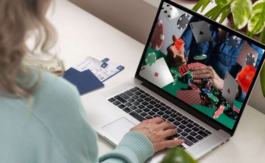 A person sitting at a desk, in front of a computer, with an online poker game on their screen. 