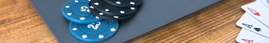 Blue and black casino chips arranged on the corner of a laptop, with playing cards arranged in front of the laptop.