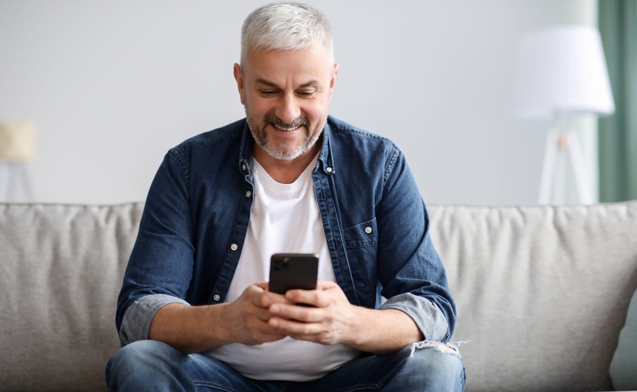 A person sitting on a couch quietly smiling while gaming on their cellphone.