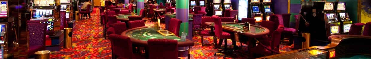 The inside of a casino with casino table games and slot machines.