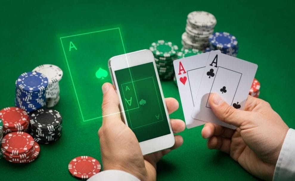 Close-up of poker player with playing cards, smartphone, and chips at green casino table