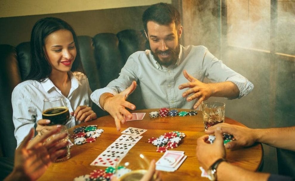 Side view photo of male and female friends sitting at wooden table playing poker