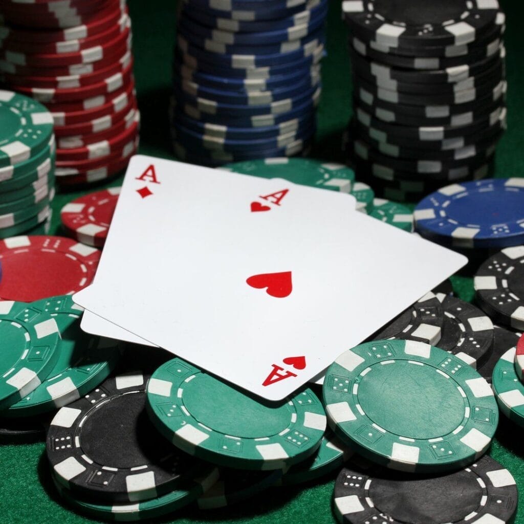 A pair of aces sitting on top of scattered poker chips. There are stacks of poker chips in the background.