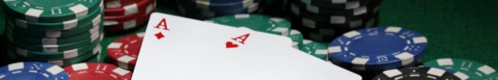 A pair of aces sitting on top of scattered poker chips. There are stacks of poker chips in the background.