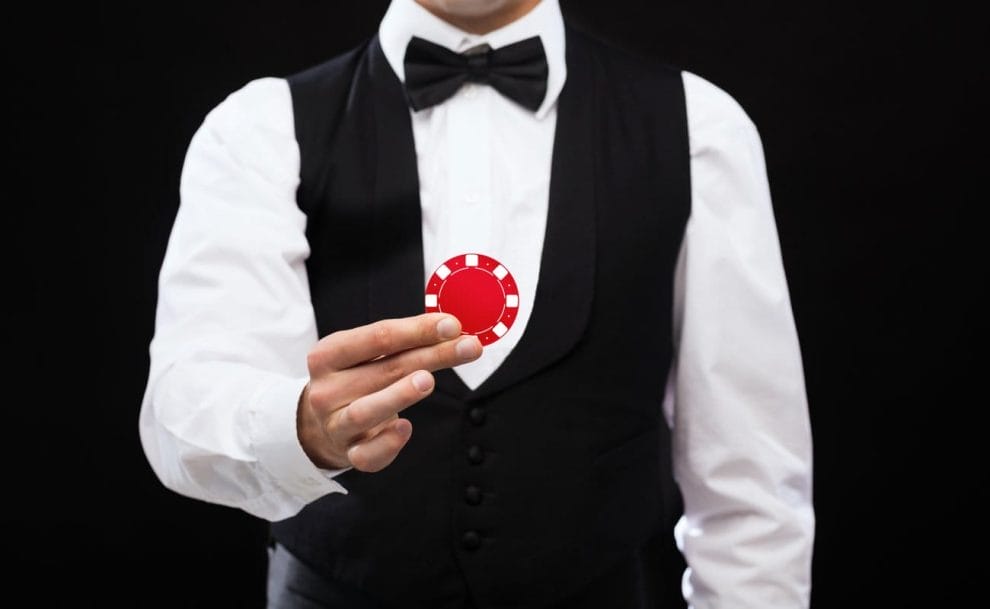 A poker dealer holds a poker chip up in front of their chest.
