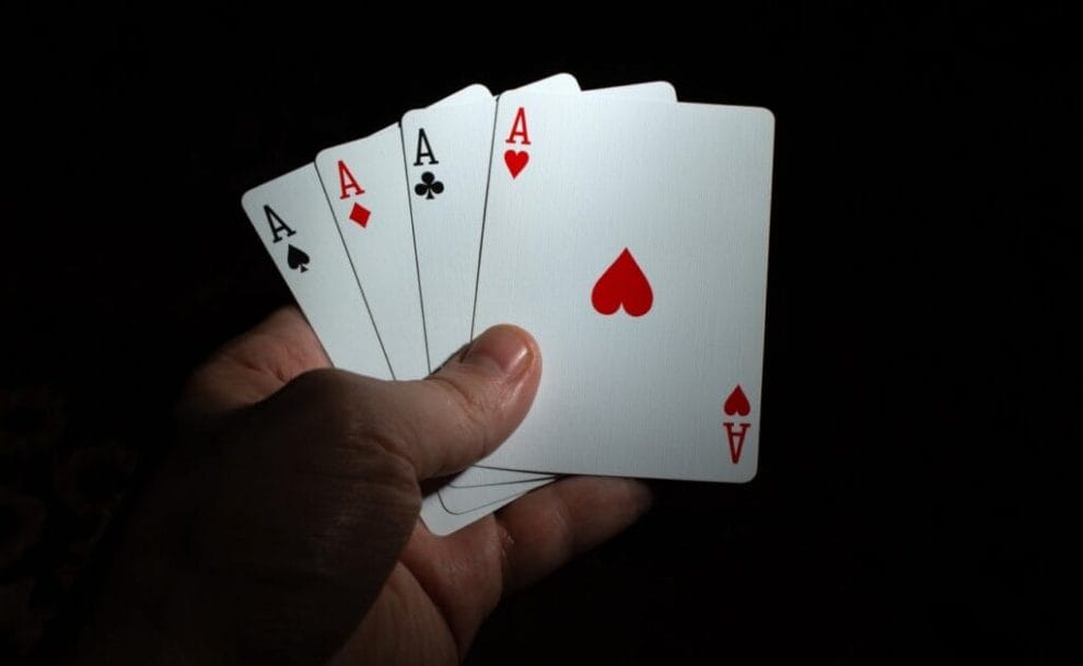 A hand holding four playing cards against a dark background.