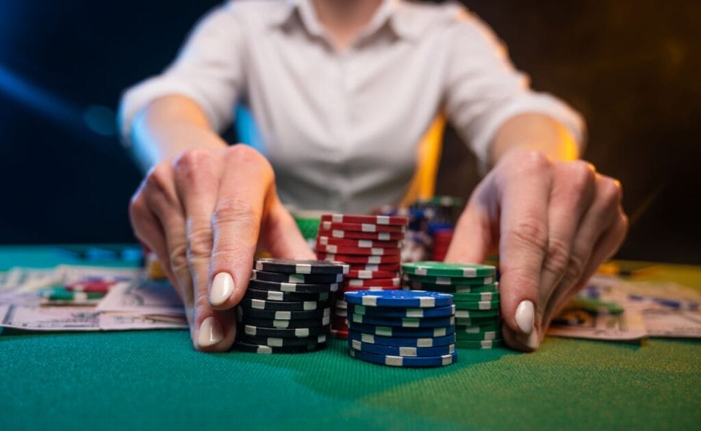 A person holding poker cards and moving chips on a green felt table.