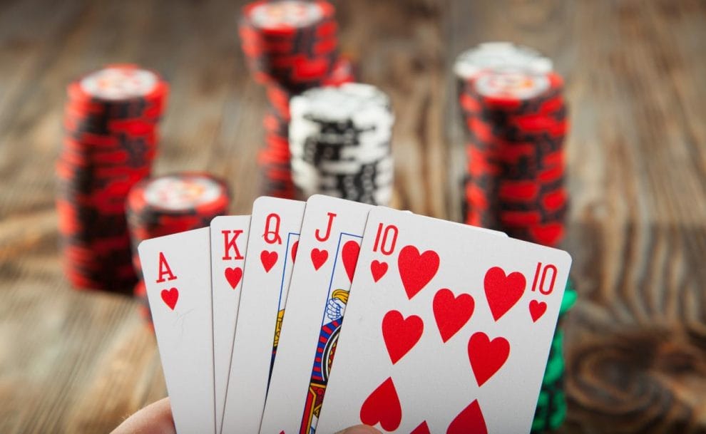 A person holds playing cards with casino chips on a wooden table.