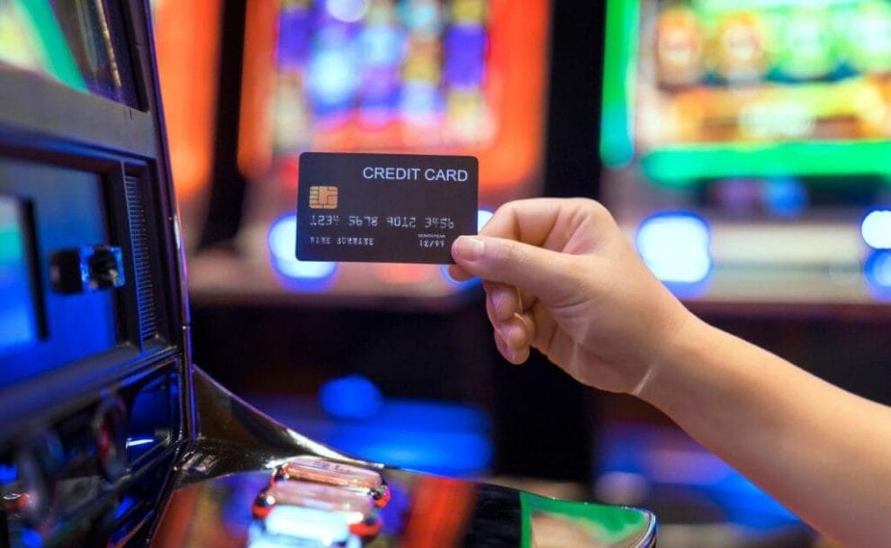 A person inserting a bank card into a slot machine inside a casino. 