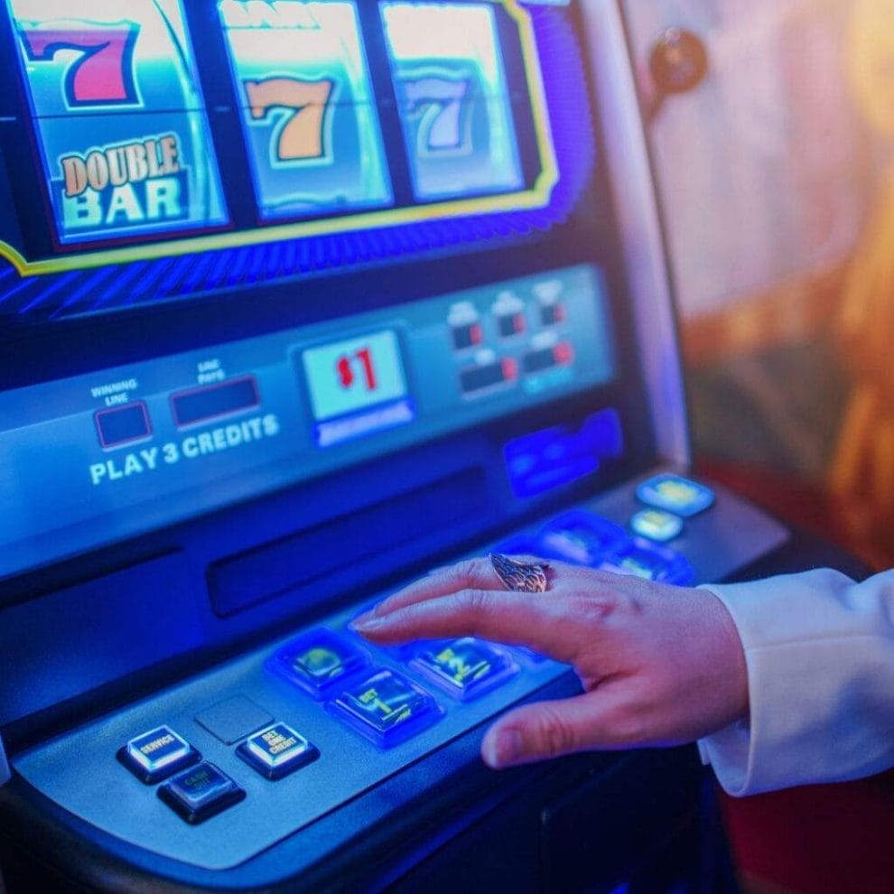 A person seated at a slot machine in a casino, poised to push a button on the machine.