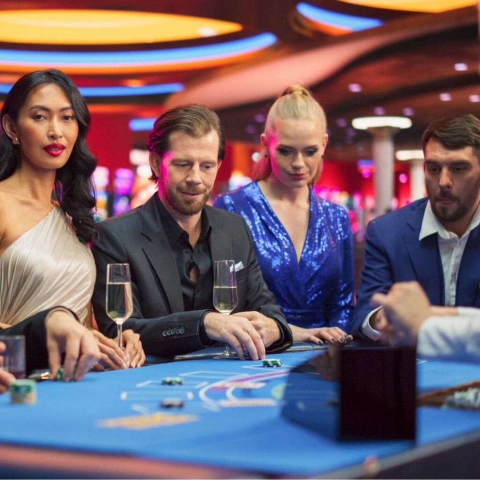 People standing around a poker table, in a casino, engaging in a game of poker.