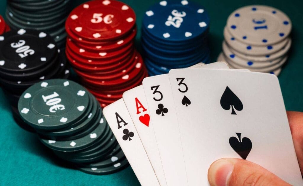 A person sitting at a poker table, holding an Ace of Clubs, an Ace of Hearts, a three of Clubs, and a three of Spades, with stacks of poker chips arranged on the table. 