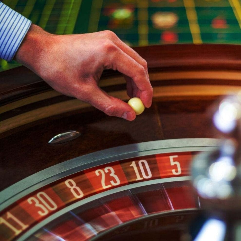 A person holding a white ball above a roulette wheel.