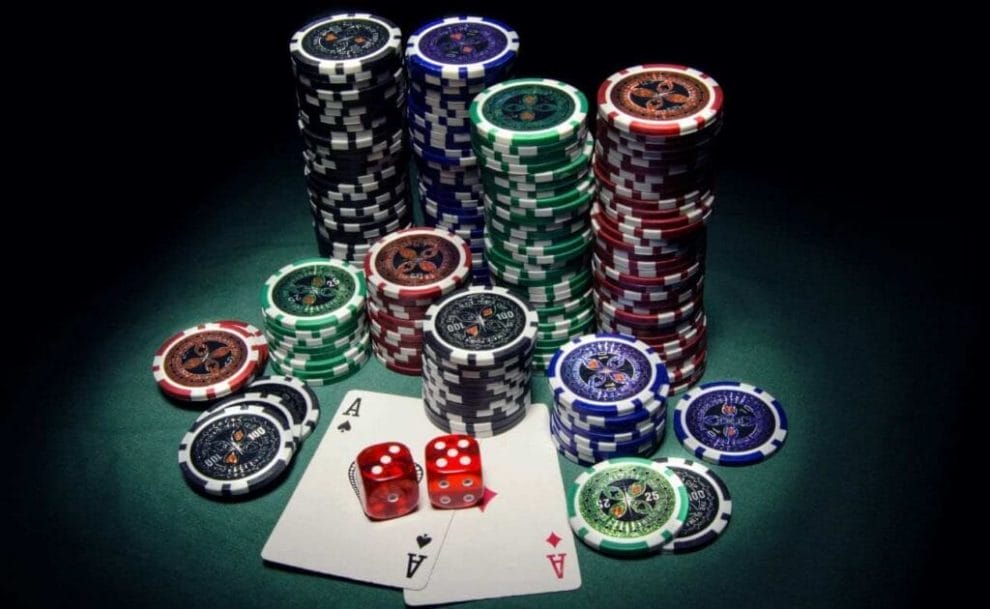 A top-down view showing a spotlight on multiple stacks of poker chips with two ace playing cards and two six sided dice in front of them.
