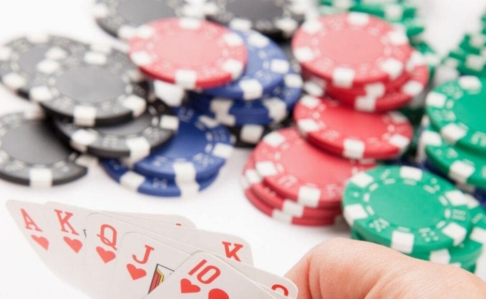 A brightly-lit image of a Royal Flush being held up with stacks of poker chips of various colors in the background.