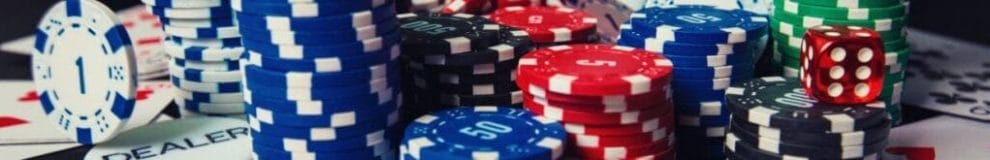 Small stacks of poker chips, a dealer chip, playing cards, and one red, six-sided dice.